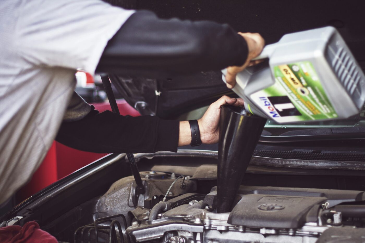 A mechanic pouring fresh Mobil 1 motor oil into a funnel set in an open engine bay